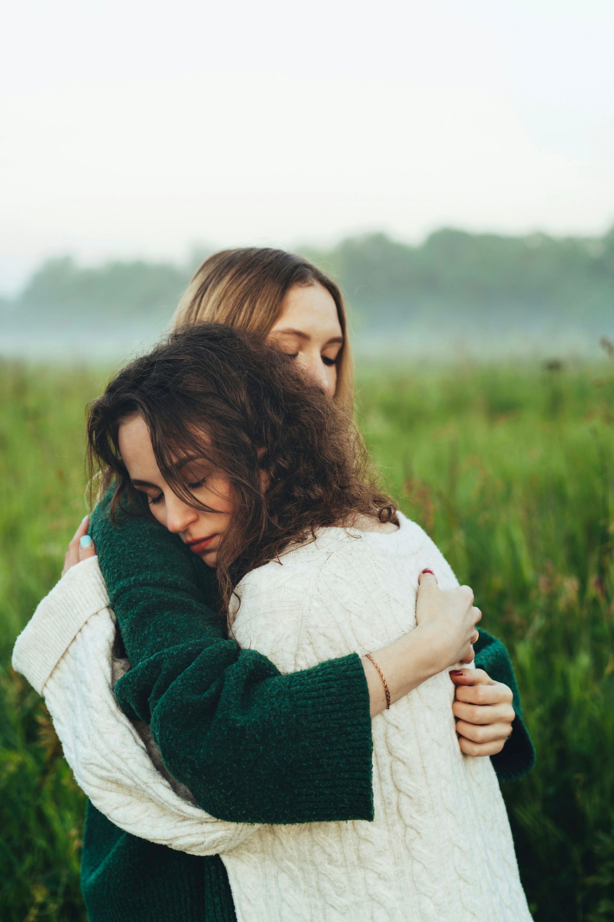 Two people hold each other in a long embrace in a misty green field.