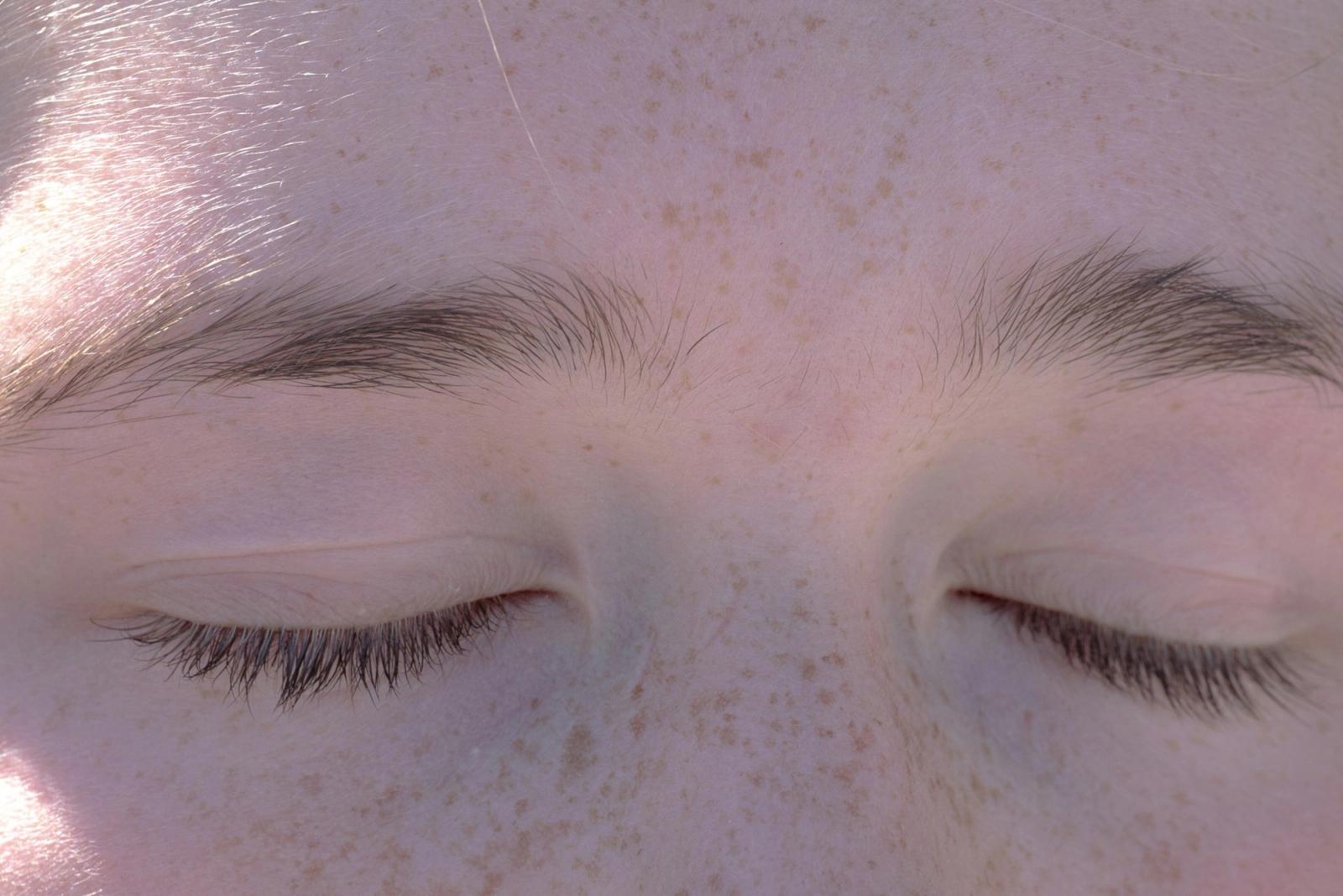 A close-up of a calm face with eyes closed in soft light.