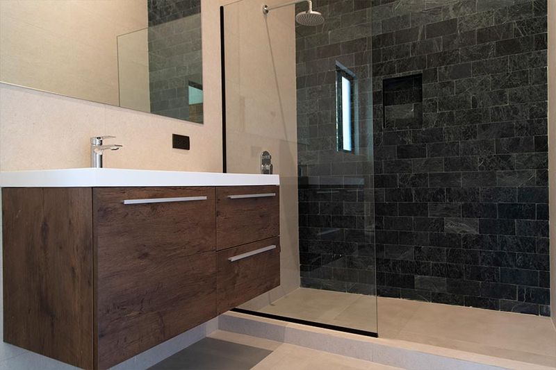 Premium bathroom with dark slate shower and warm-wood vanity.