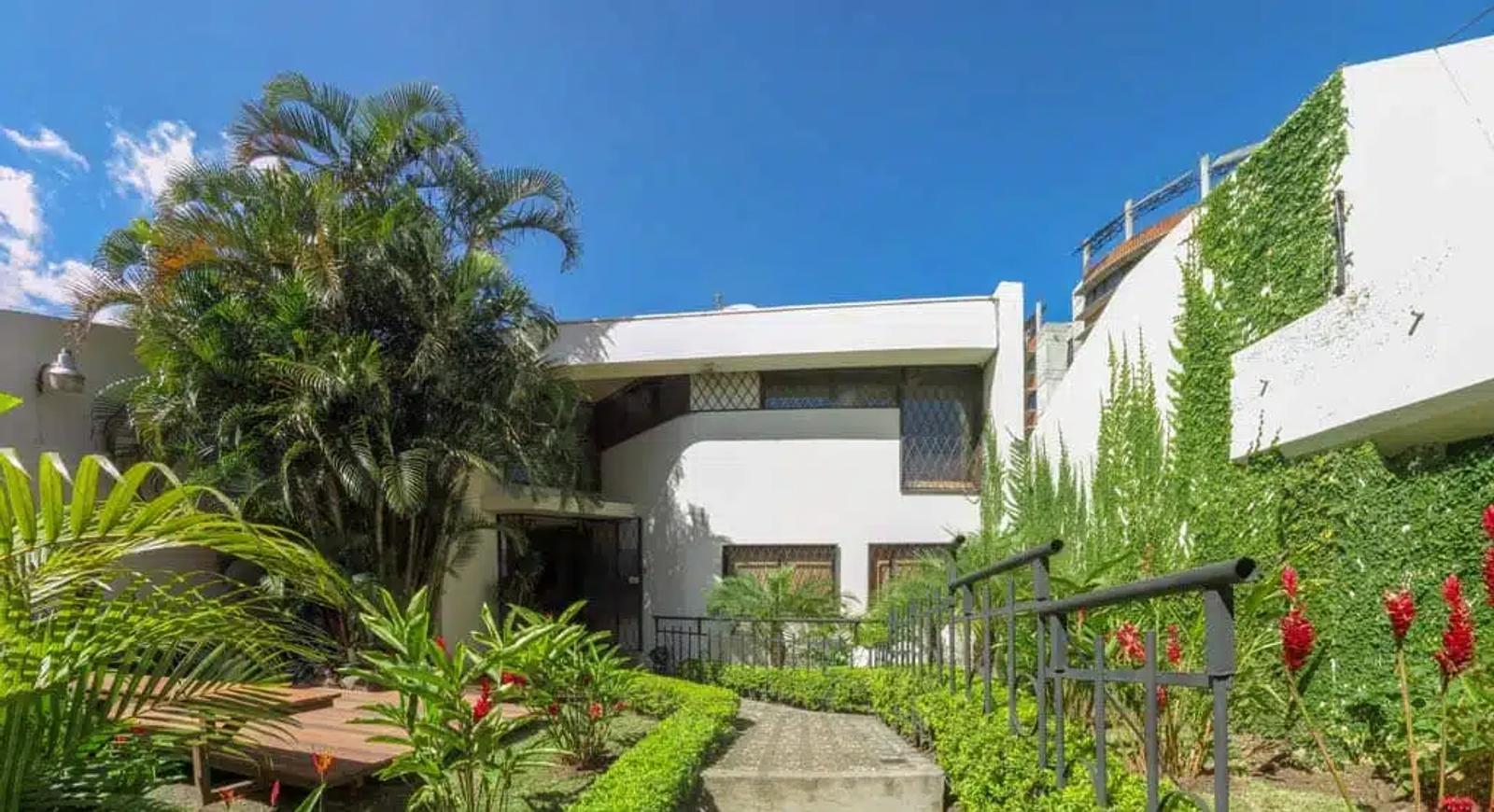 Garden entrance to the CRTC San José residence, with palm and tropical planting framing a discreet white facade.
