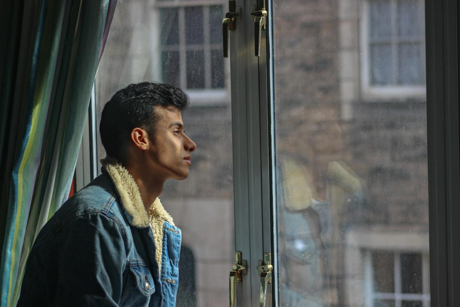 A person sitting in profile, looking out a window in quiet reflection.