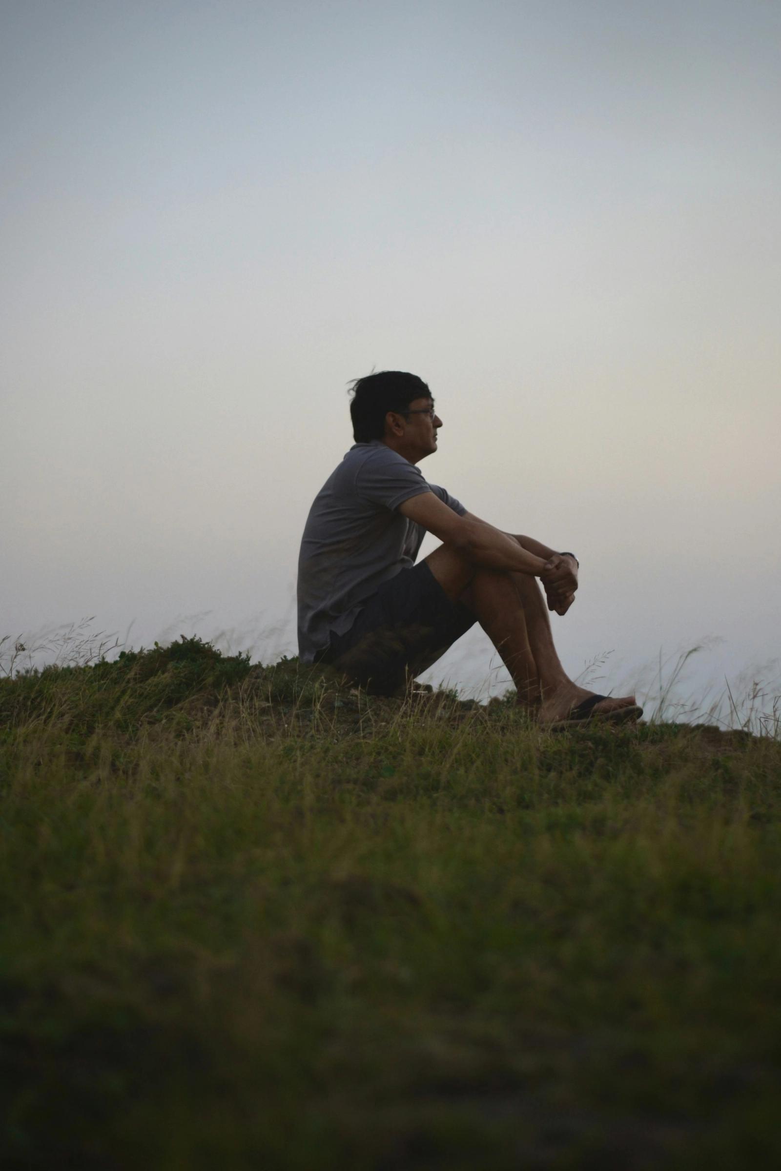 A person sitting on a grassy hill, looking out at an open sky.