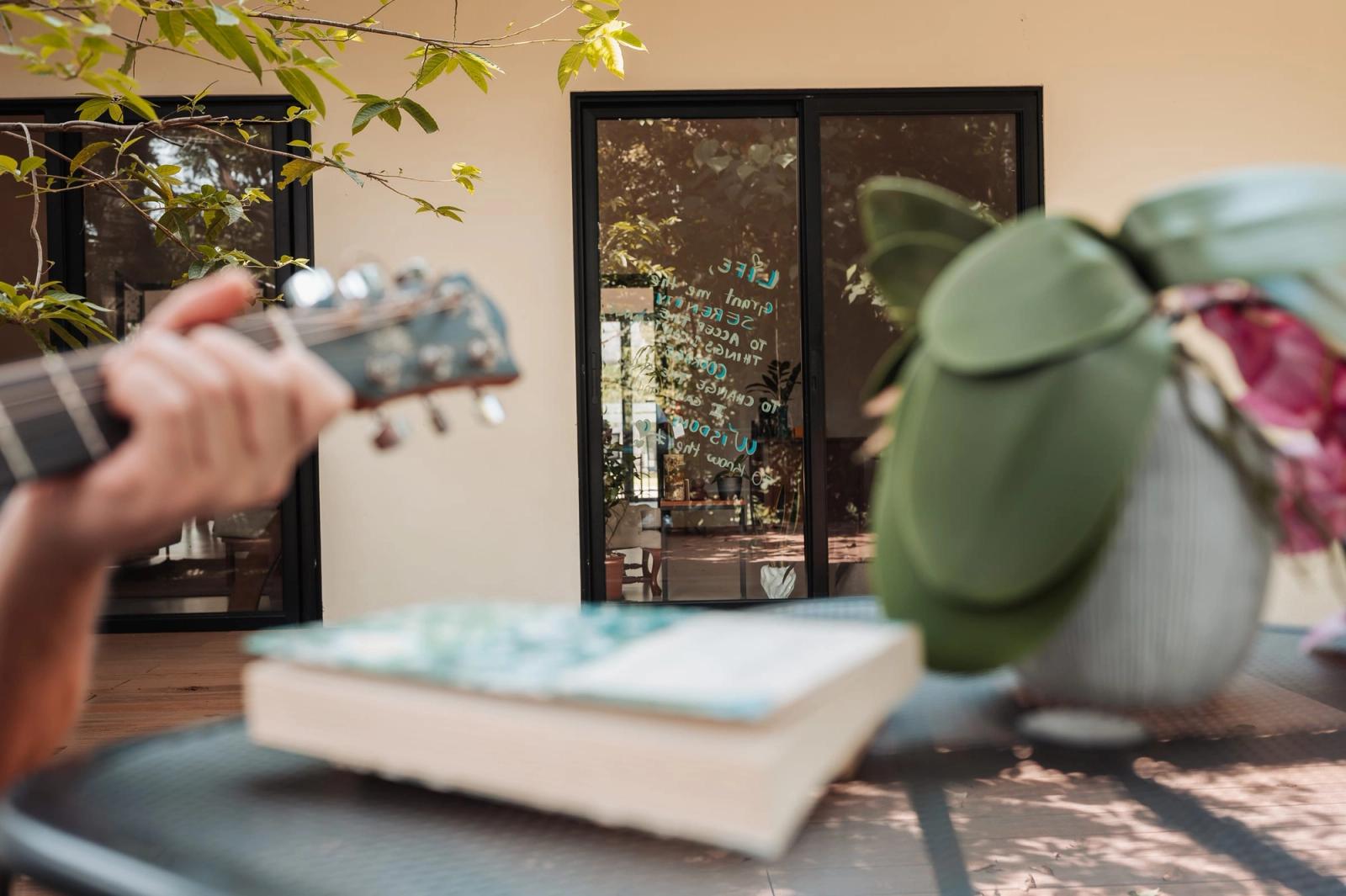Una guitarra y un libro abierto en una mesa del porche, con la casa y el jardín detrás.