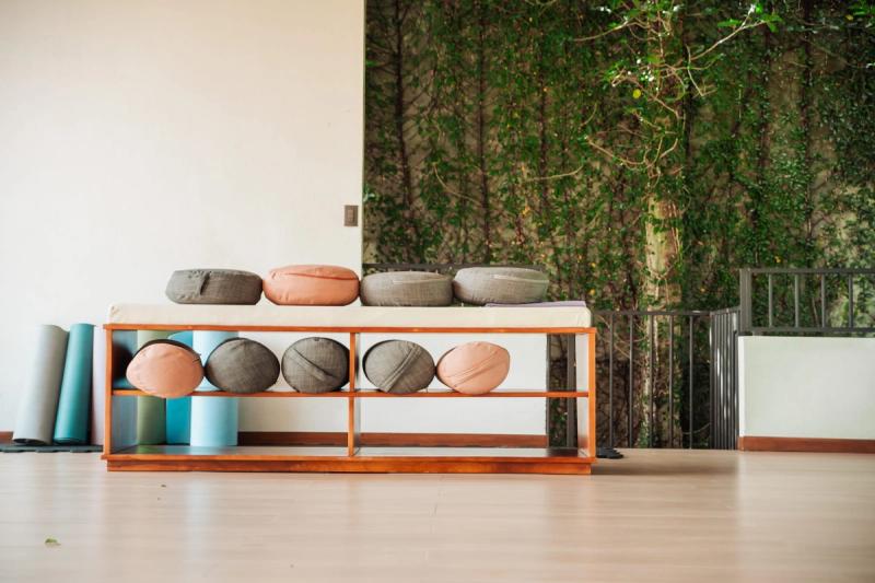 Meditation cushions and rolled yoga mats on a wooden bench in the open-air yoga hall, with a wall of greenery behind.