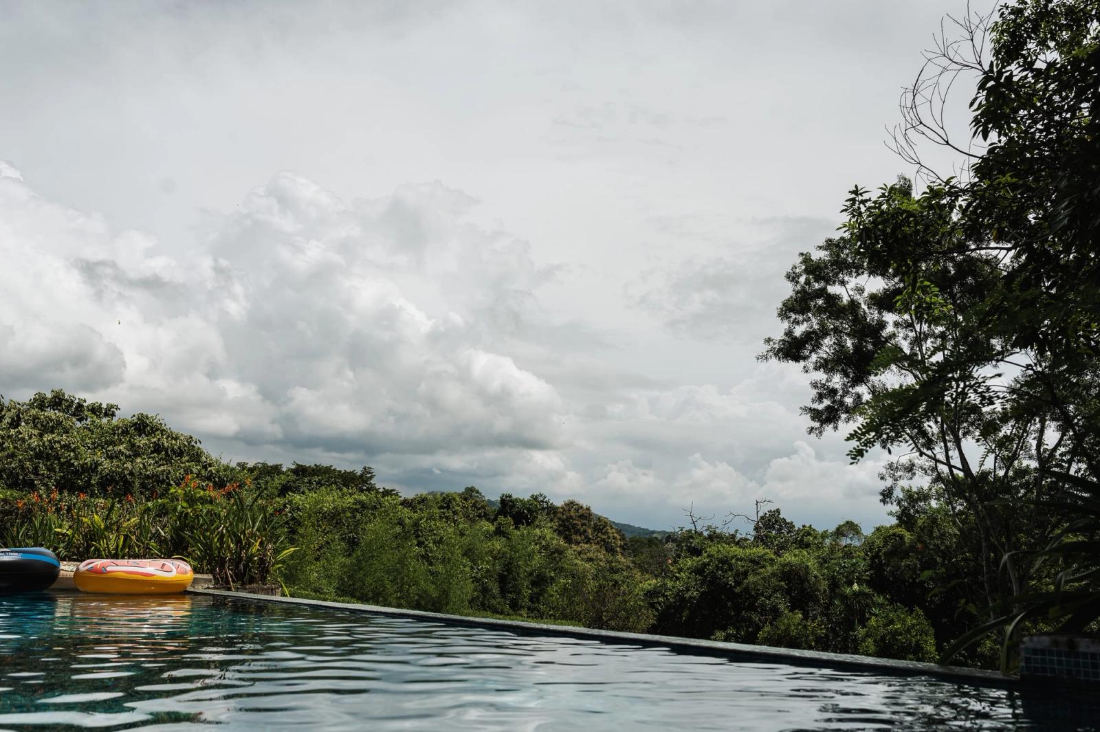 The edge of the infinity pool meeting the treetops and a cloudy sky.