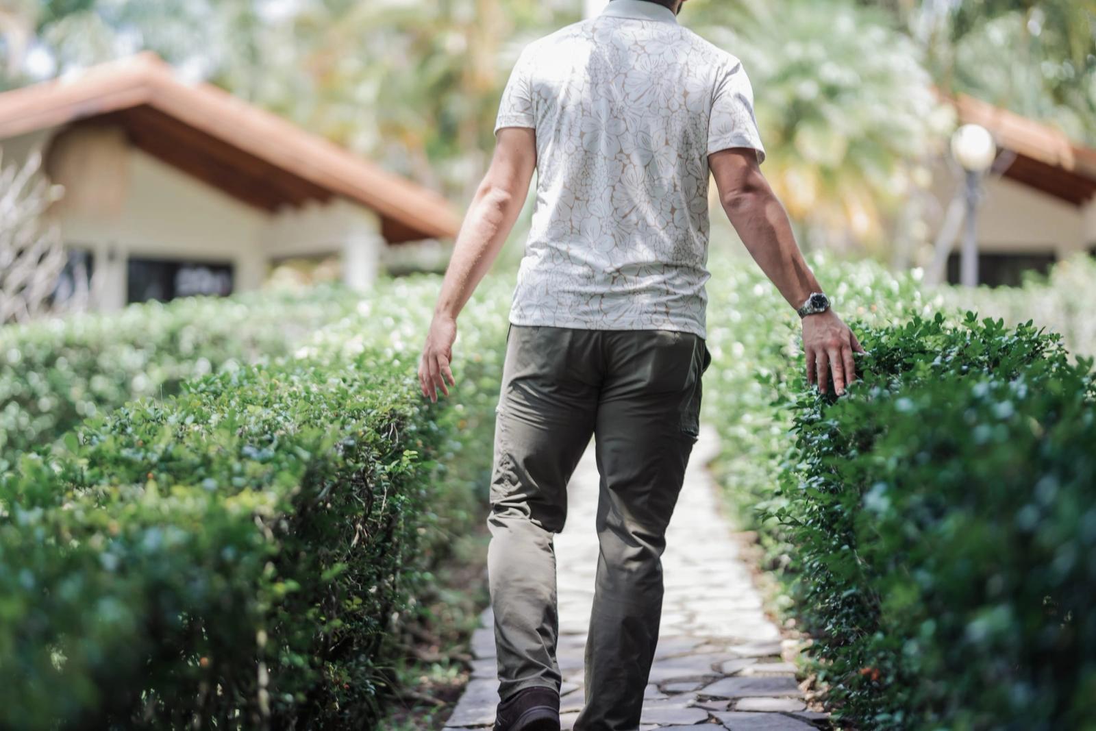 A man walking a garden path between low hedges, trailing a hand through the leaves.