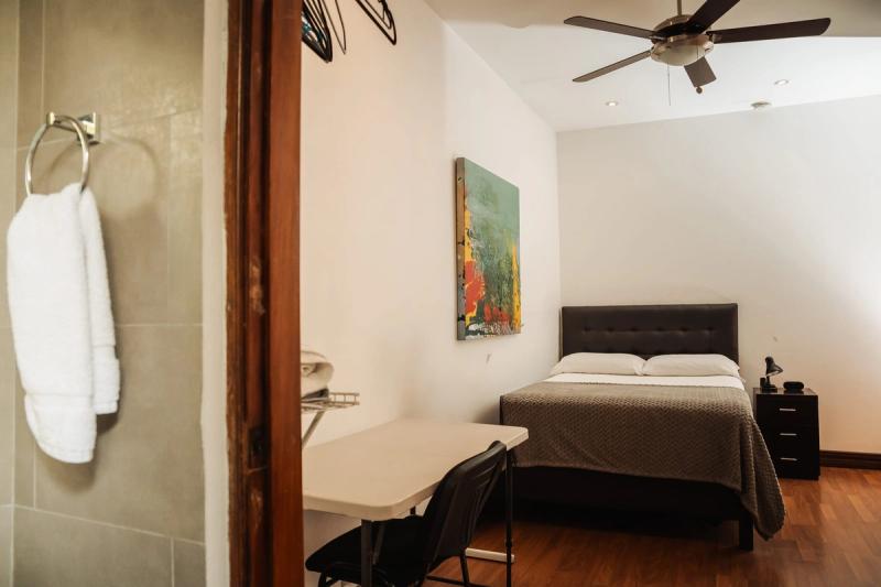 A private room at San José with a double bed, a desk and a painting, seen from the bathroom door.