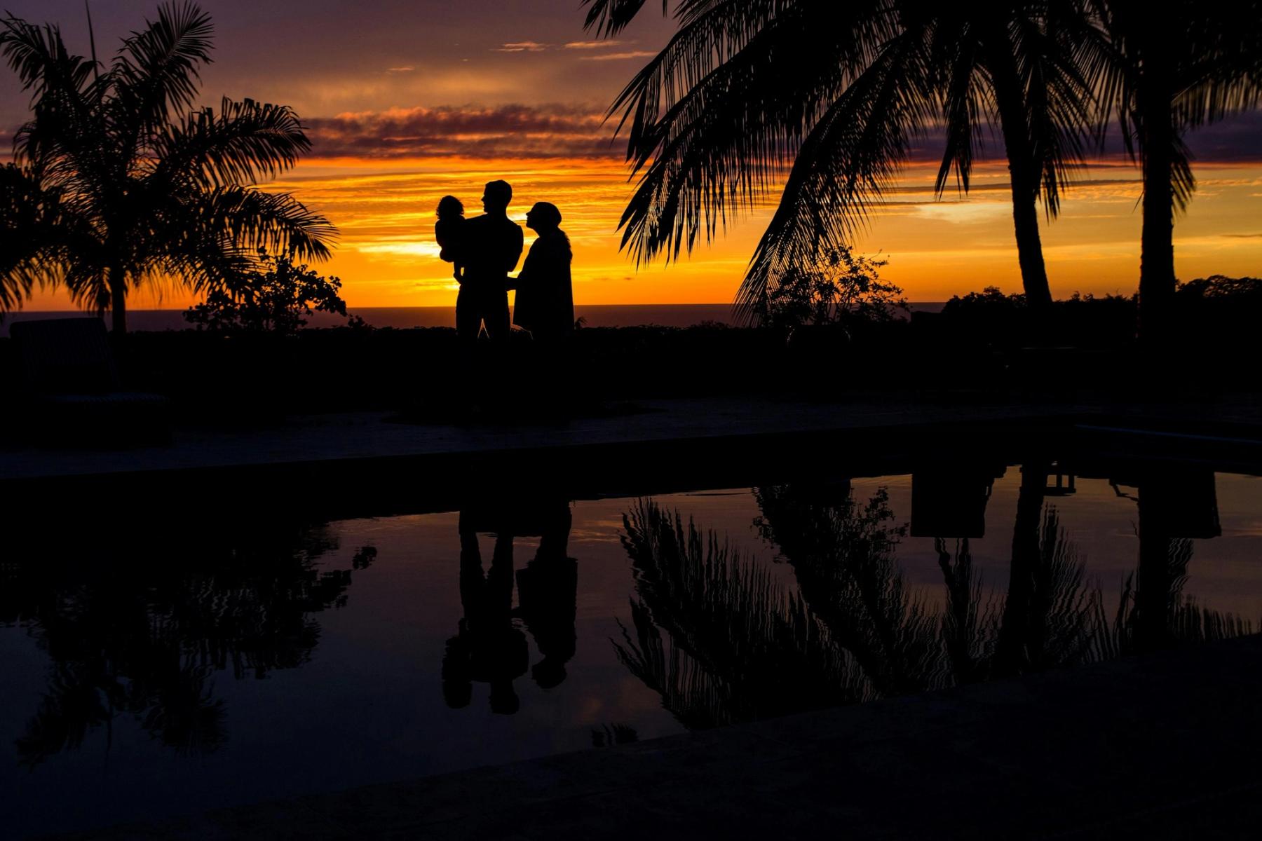 A family of three silhouetted against a warm sunset.
