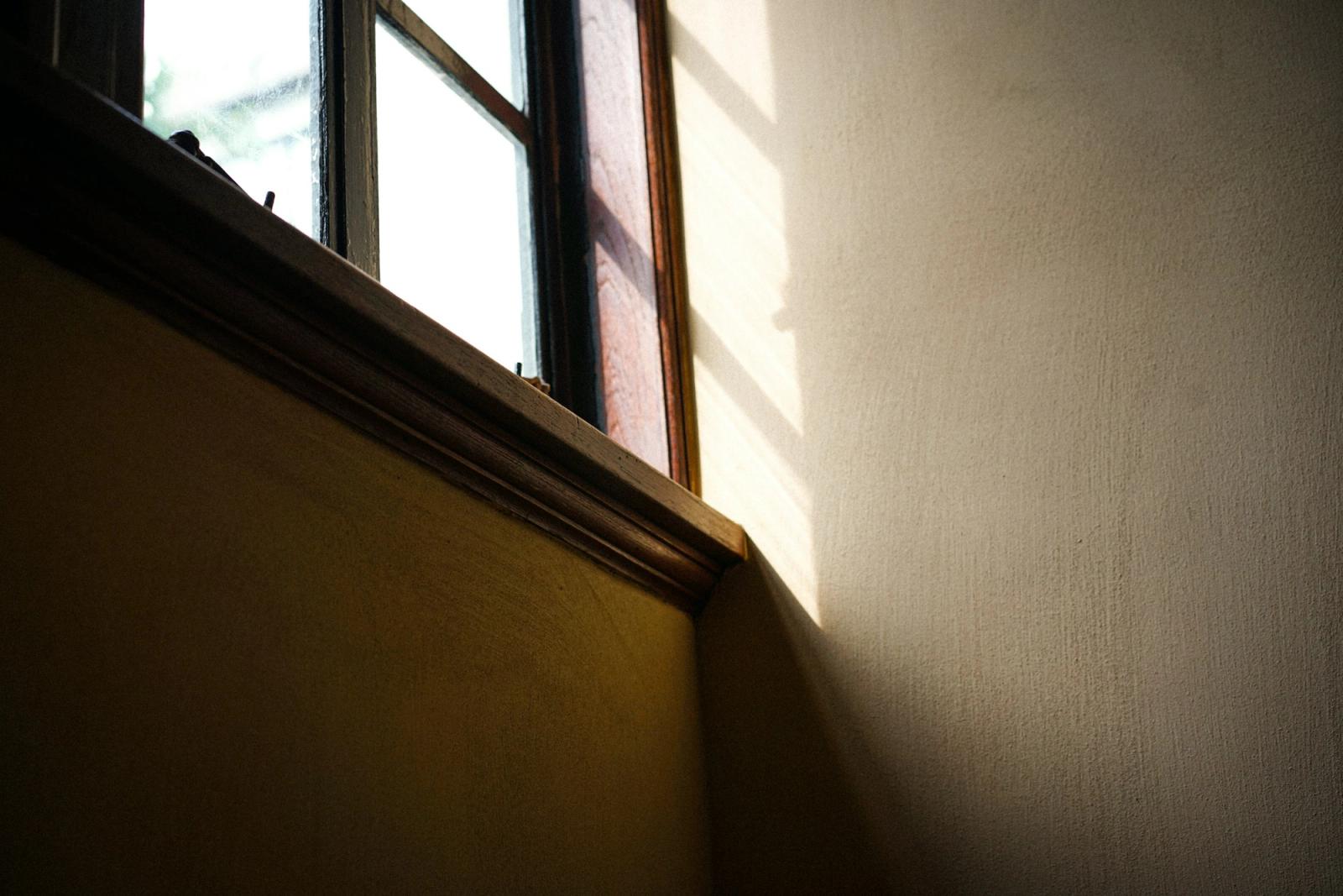 Warm daylight falls through a wooden window frame onto a quiet, light-colored wall.