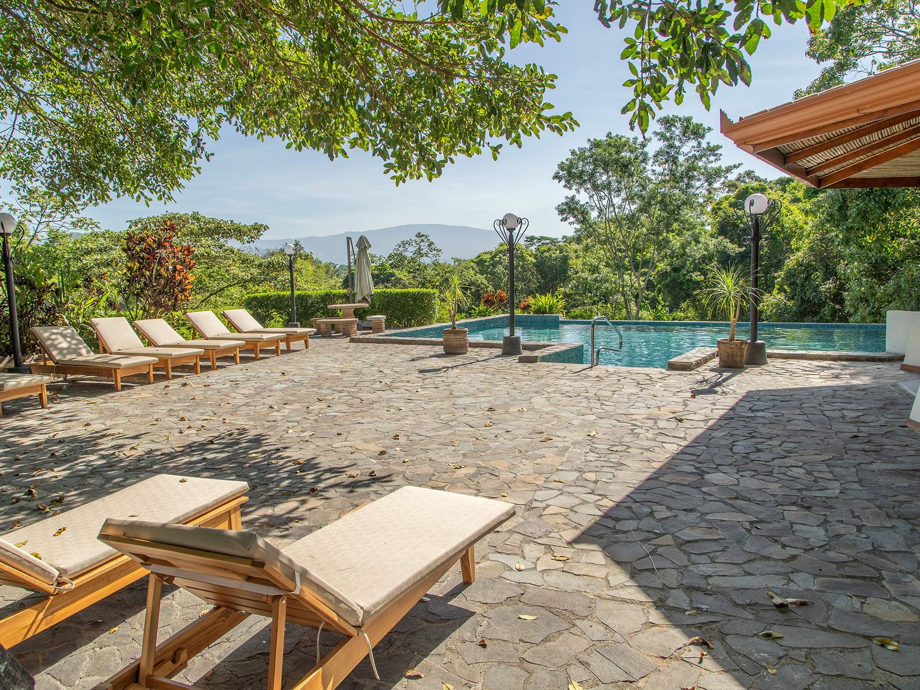 Stone-paved pool terrace at Riverside with loungers facing the mountain forest of the Atenas valley.