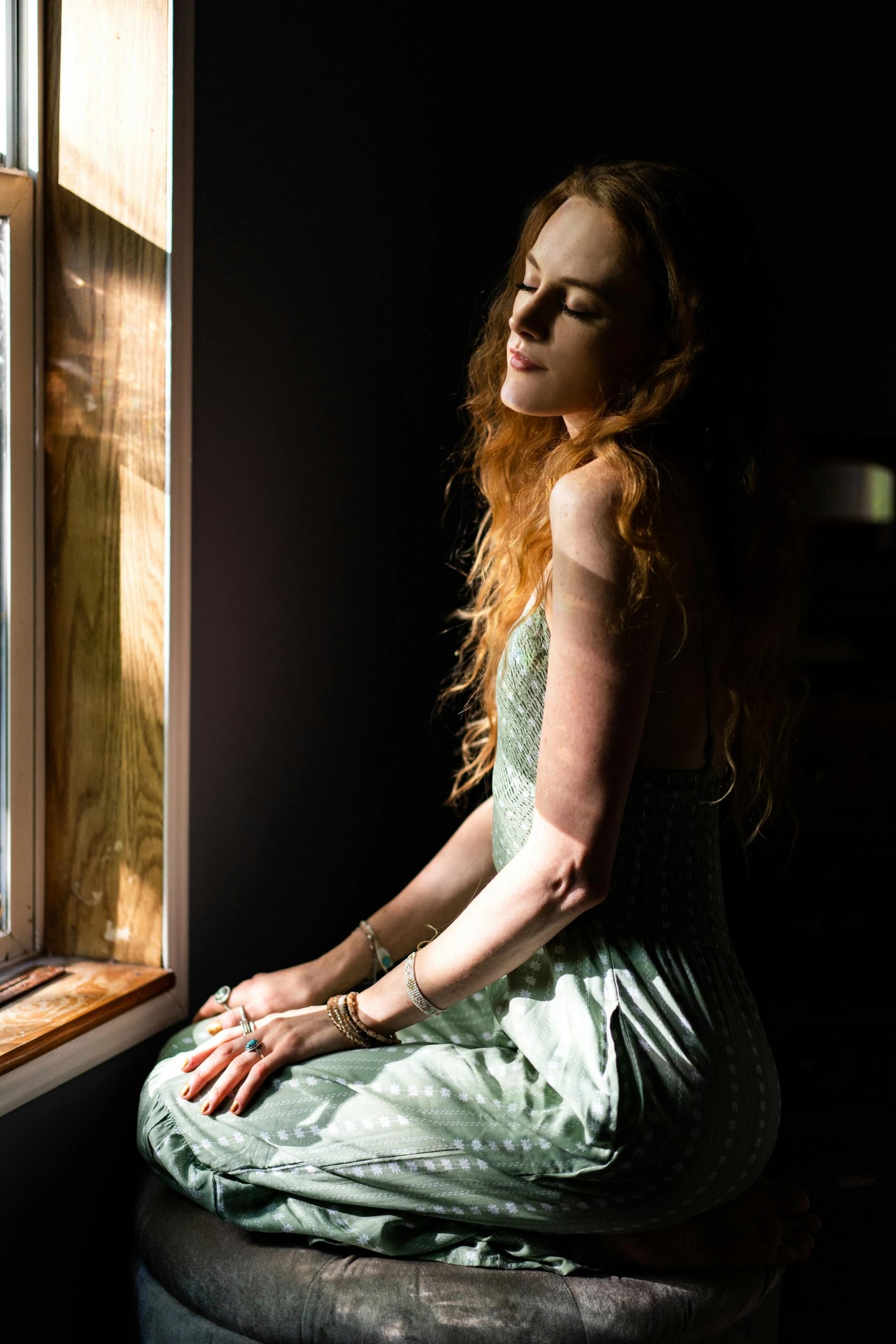 A person sitting by a window in soft, warm light, looking out.