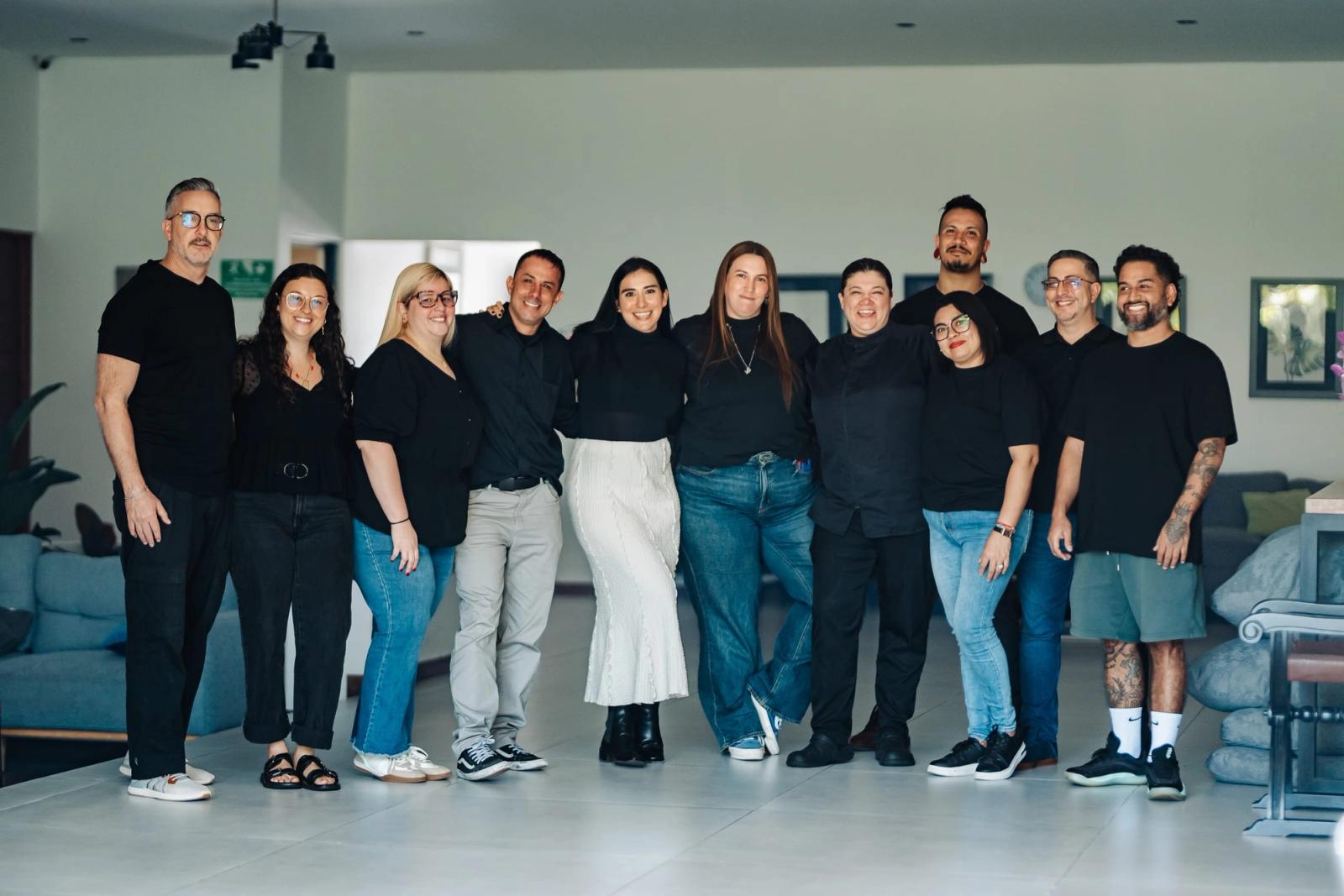 The CRTC team, about a dozen people in black, standing together in the living room at San José.
