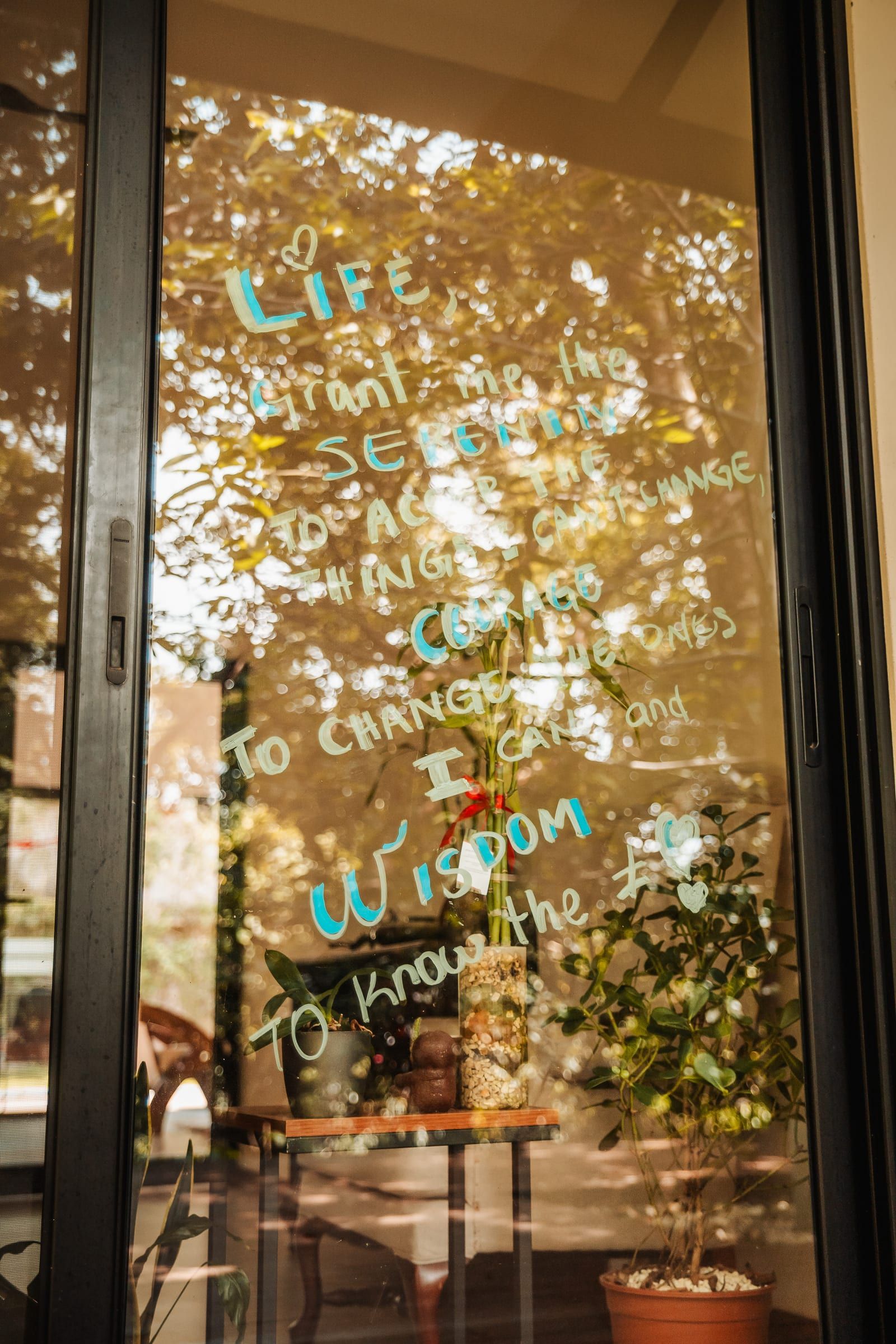 Palabras escritas con marcador en una puerta de vidrio, con el comedor y el jardín detrás.