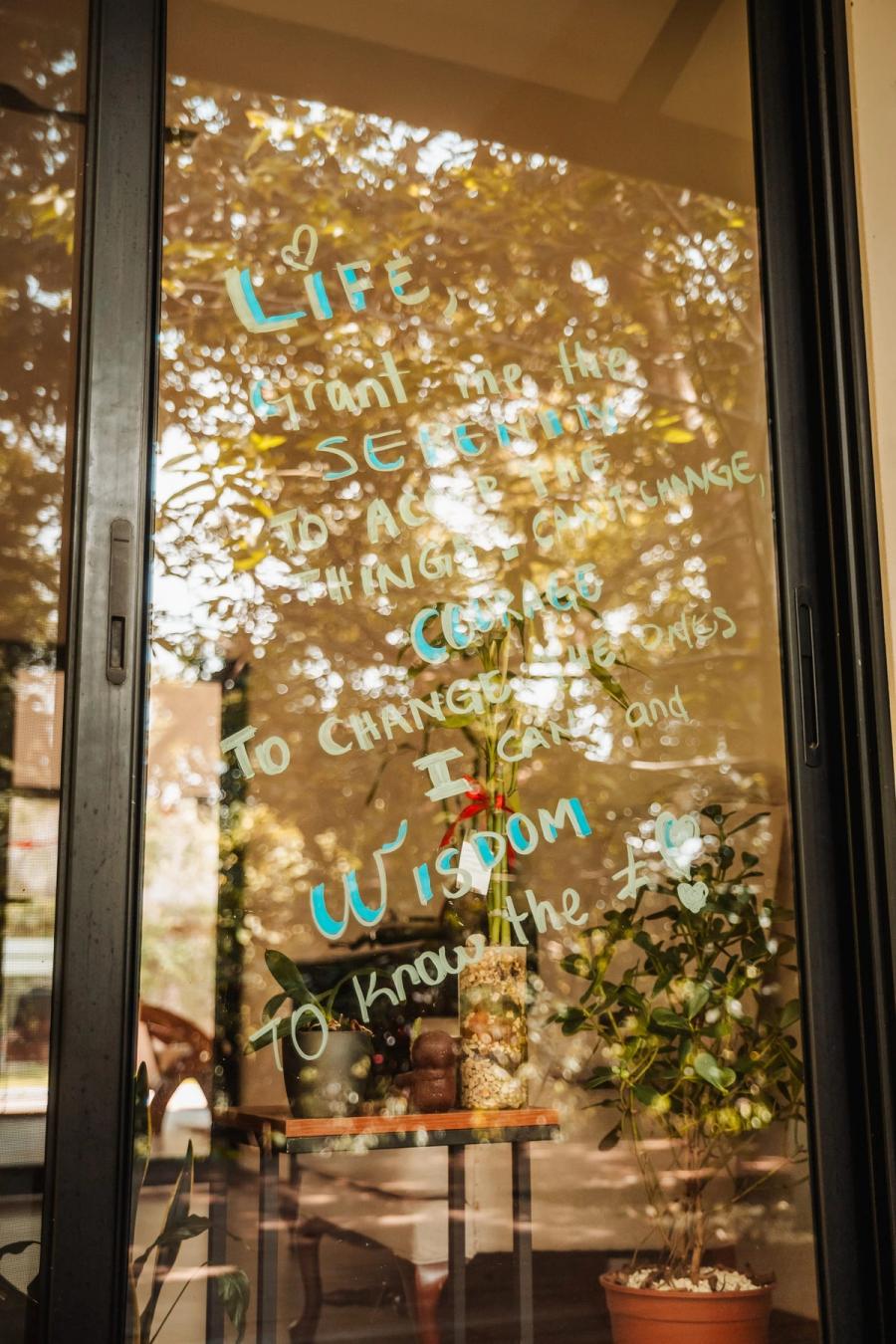 Words written in marker on a glass door, with the dining room and garden beyond.