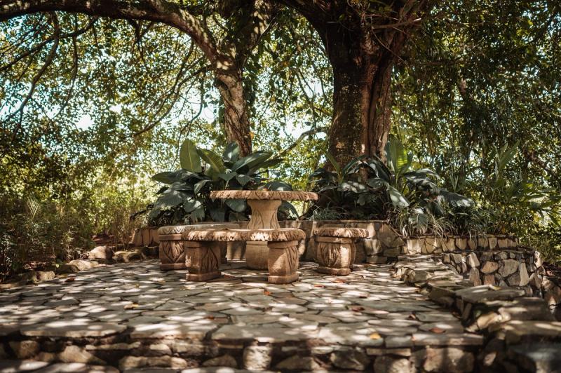 A carved stone table and benches on a flagstone patio under a large tree.