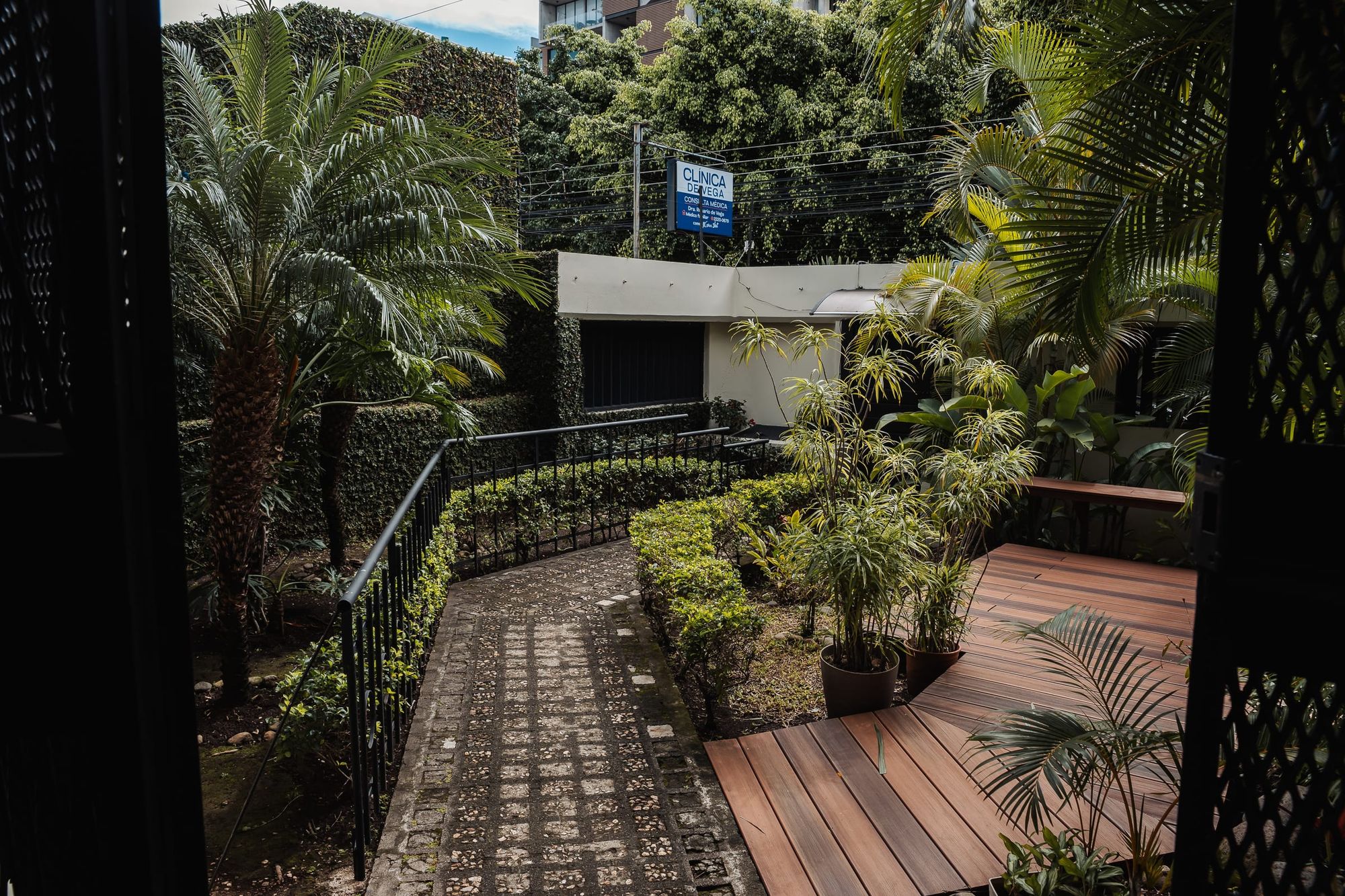 Un sendero de baldosas y una terraza de madera entre el jardín sembrado de la residencia de San José.
