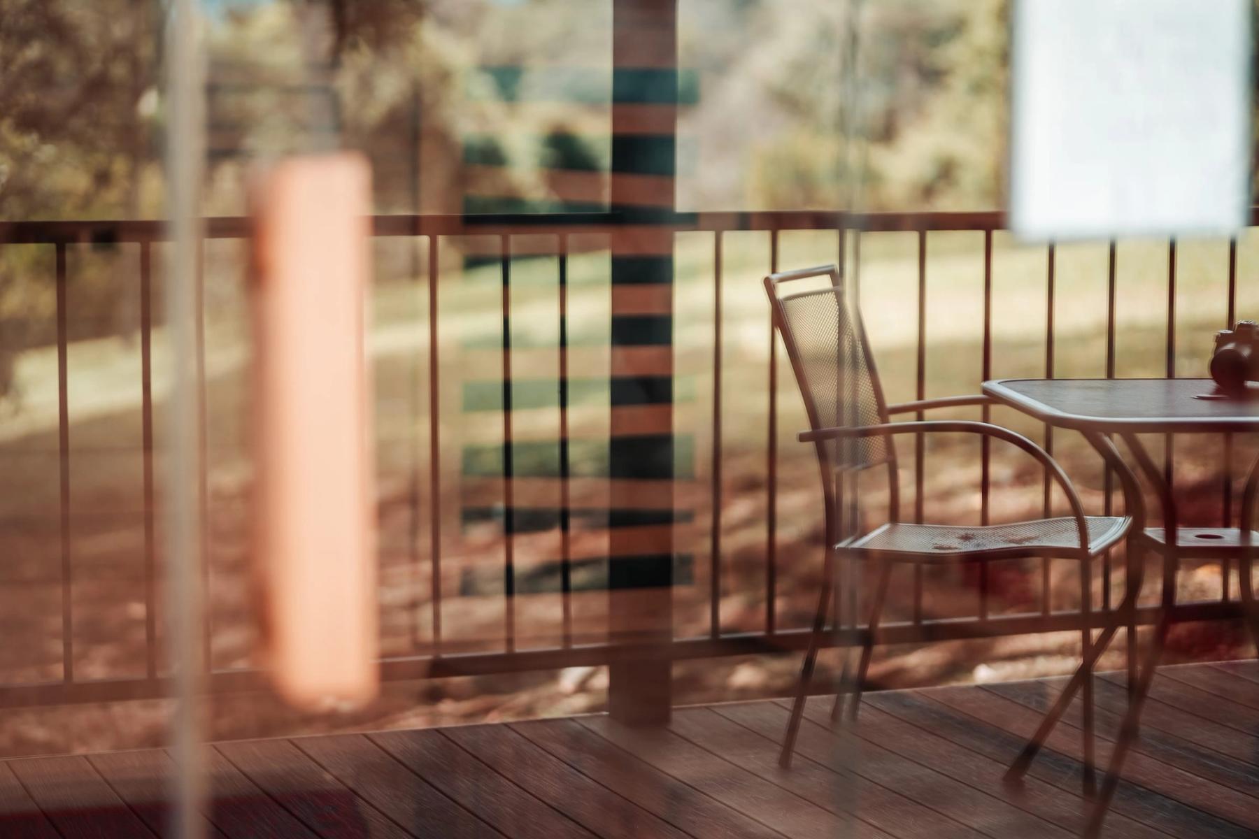 Una mesa pequeña y una silla en una terraza de madera con vista a una ladera verde.