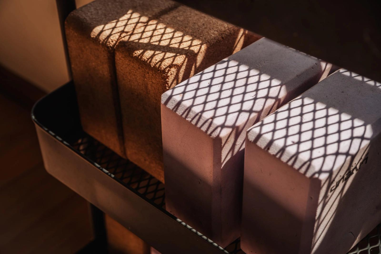 Cork yoga blocks on a shelf, crossed by a lattice of afternoon shadow.