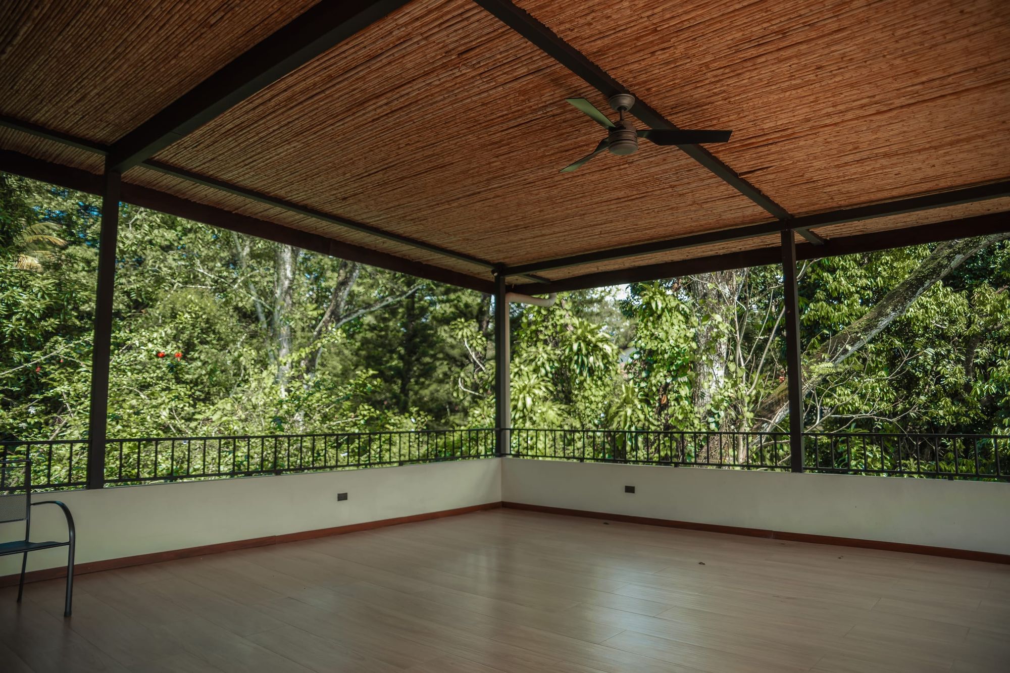 The empty yoga hall under its bamboo ceiling, with ceiling fans and a railing that opens onto dense forest.