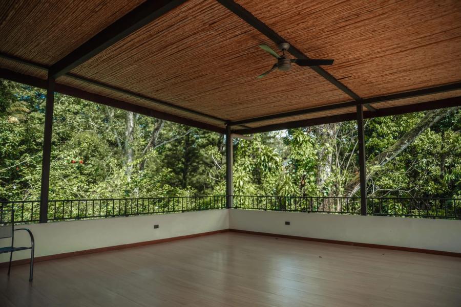 The empty yoga hall under its bamboo ceiling, with ceiling fans and a railing that opens onto dense forest.