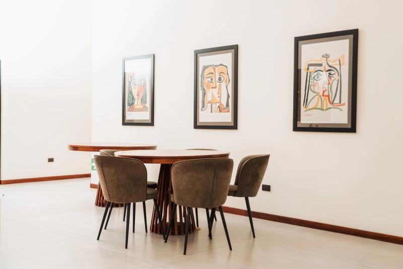 The dining room at Atenas: round wooden tables, upholstered chairs and framed prints on a white wall.