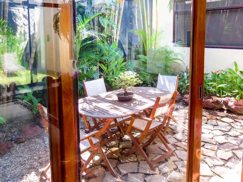 Small interior courtyard at the San José residence with a folding-table setting under tropical planting, framed by sliding glass doors.