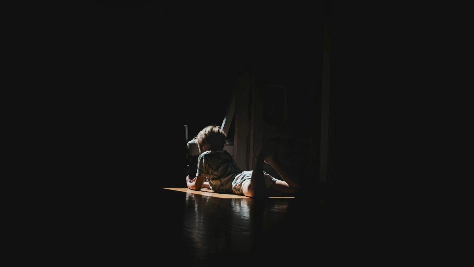 A person resting on a wooden floor in a soft pool of light.