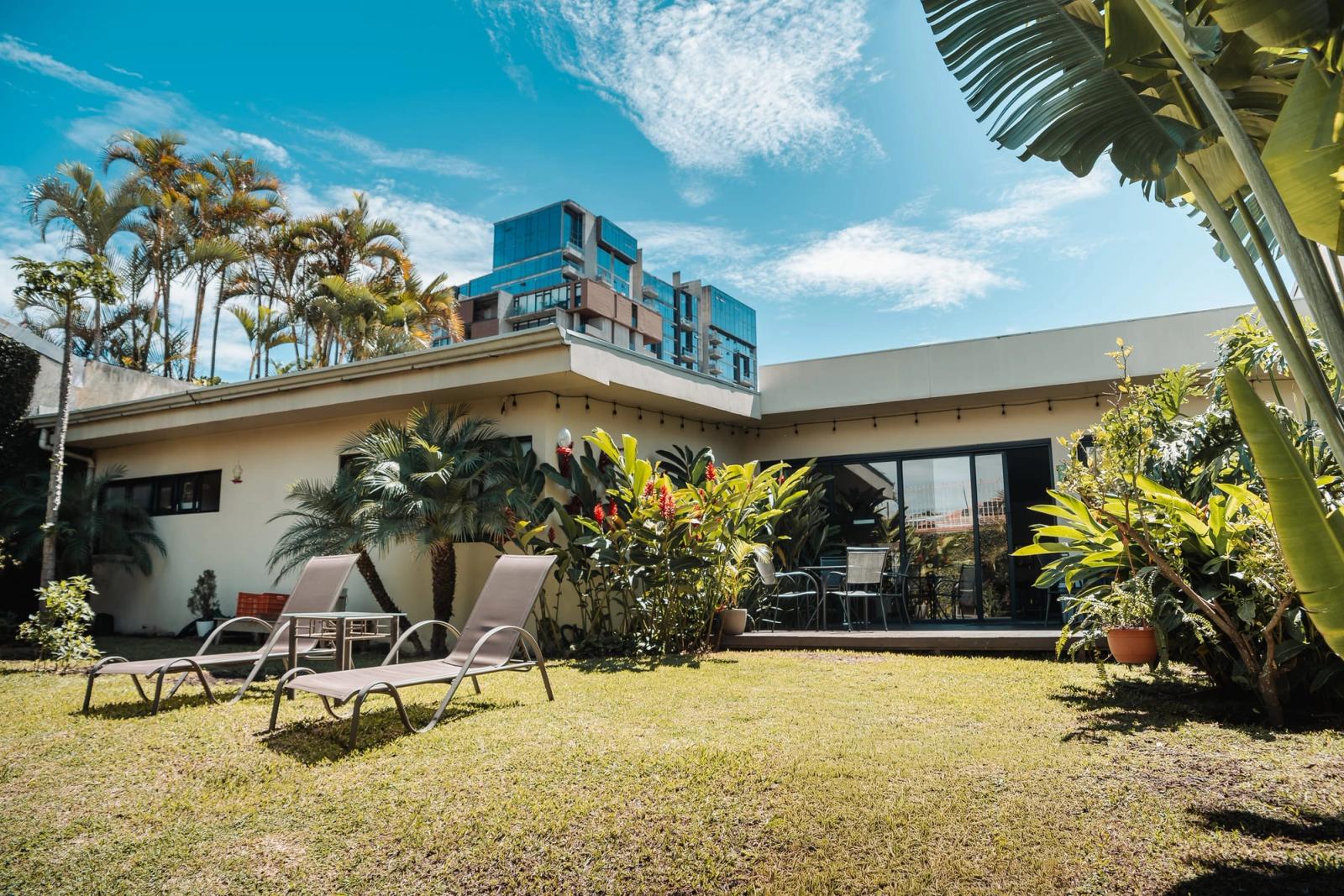 The garden at the San José residence, with sun loungers on the lawn in front of the house under a clear blue sky.