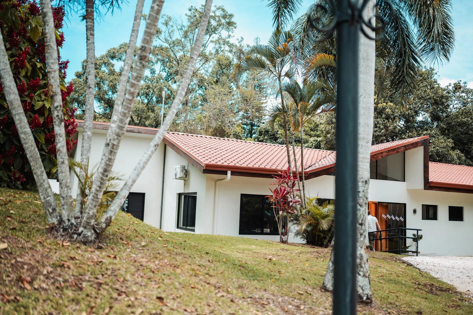 The main house at Atenas: white walls and a red tiled roof among tall palms and a sloping lawn.
