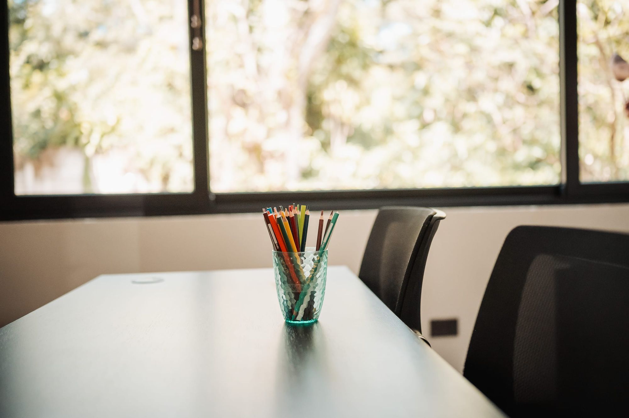 A cup of colored pencils on a group-room table beside a window onto the garden.