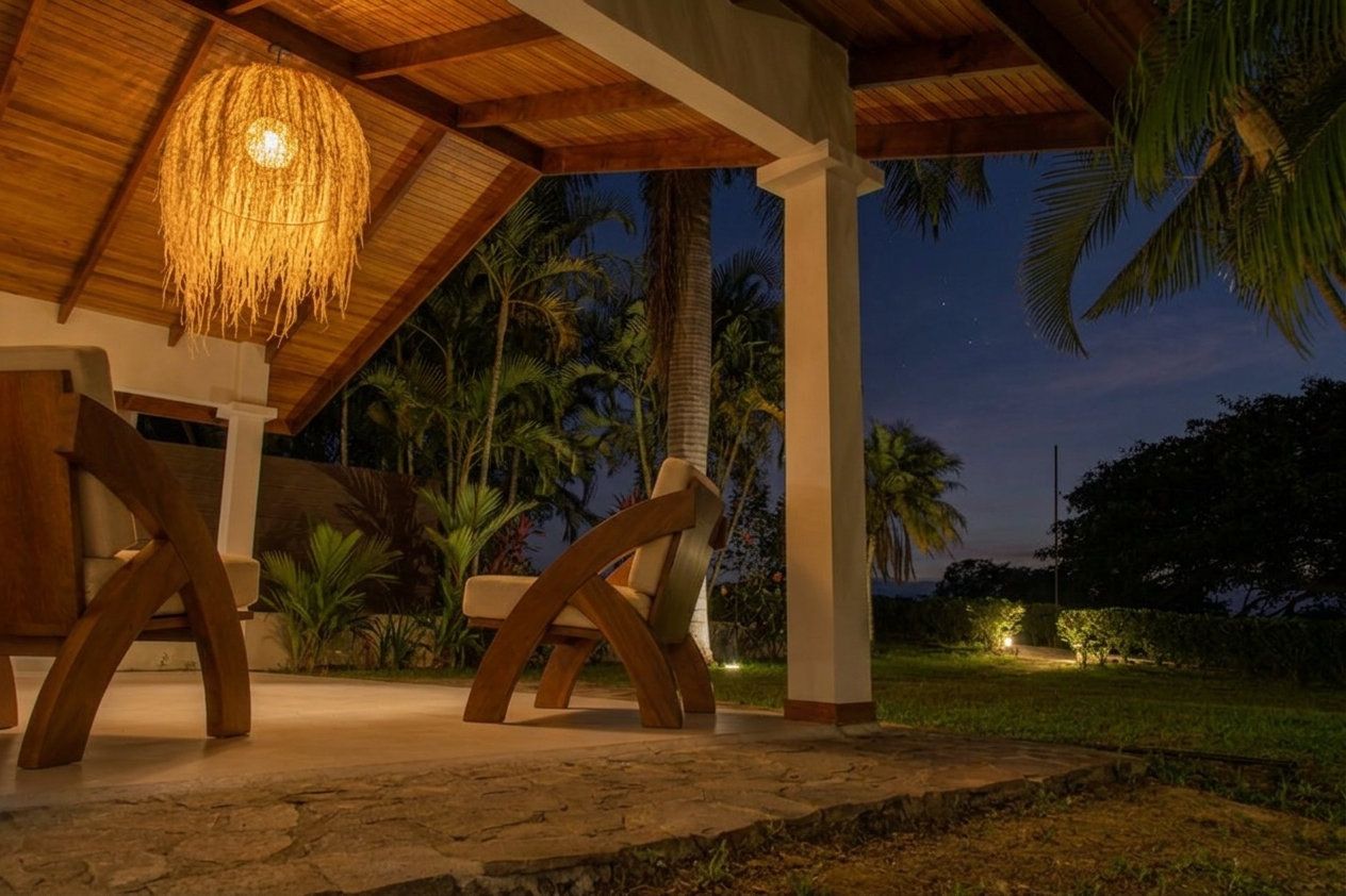 A covered terrace at the center at dusk, with warm lighting and wooden chairs.