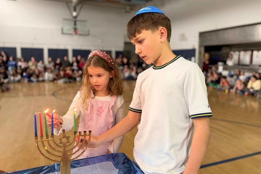 Two Senesh students light a menorah for Hanukkah together during an assembly.
