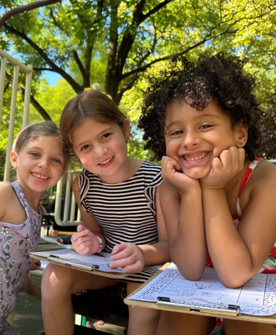 Three Senesh students smiling and sketching outside on the playground.