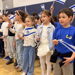 A group of Senesh students smiling and waving Israeli flags.