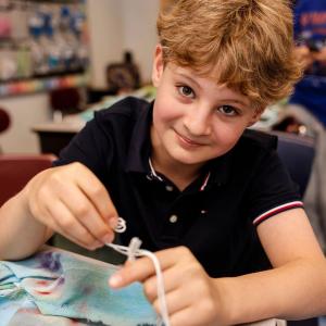 Senesh student tying their own tzitzit (fringes) on a tallit (Jewish prayer shawl).