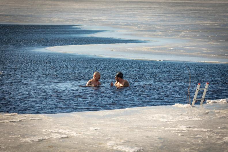 Two men enjoying a cold plunge in an icy lake, surrounded by frozen water during the practice of cold water immersion.