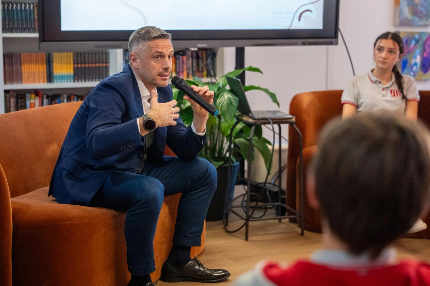 A guest speaker with a microphone talking to ISS students in the school library