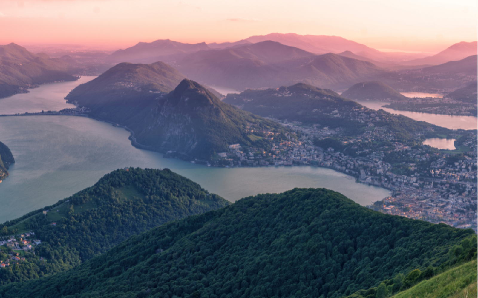 Lake Lugano and the surrounding mountains at dusk, seen from above