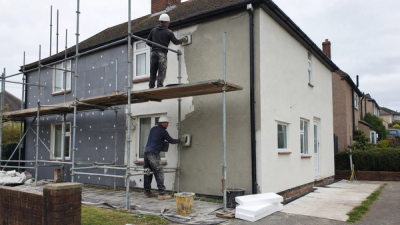 Professional home energy assessor completing a heat loss survey in a British living room with radiator measurements and insulation notes.