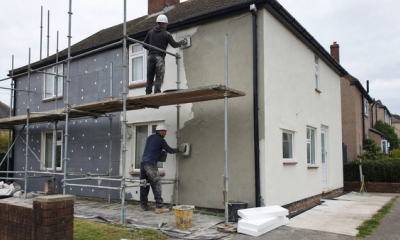 Professional home energy assessor completing a heat loss survey in a British living room with radiator measurements and insulation notes.