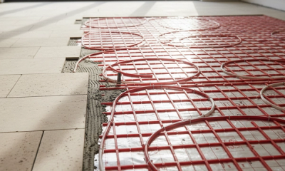 A UK living room floor under construction with wet underfloor heating pipework laid in red protective panels over insulation, ready for screed and tile finish.