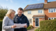 Homeowner and energy advisor reviewing solar panel grant paperwork outside a UK home with rooftop solar panels.