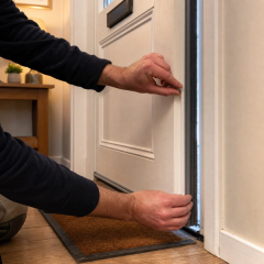 Installer fitting a draught seal to a front door in a UK home.