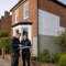 A qualified installer and energy assessor reviewing solid wall insulation on a tidy British brick home in 2026, with external insulation preparation visible on one wall.