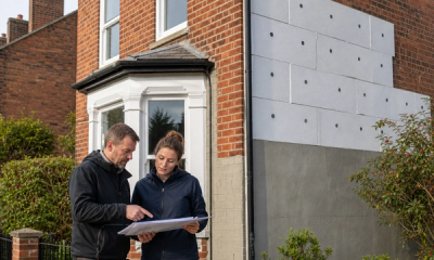 A qualified installer and energy assessor reviewing solid wall insulation on a tidy British brick home in 2026, with external insulation preparation visible on one wall.