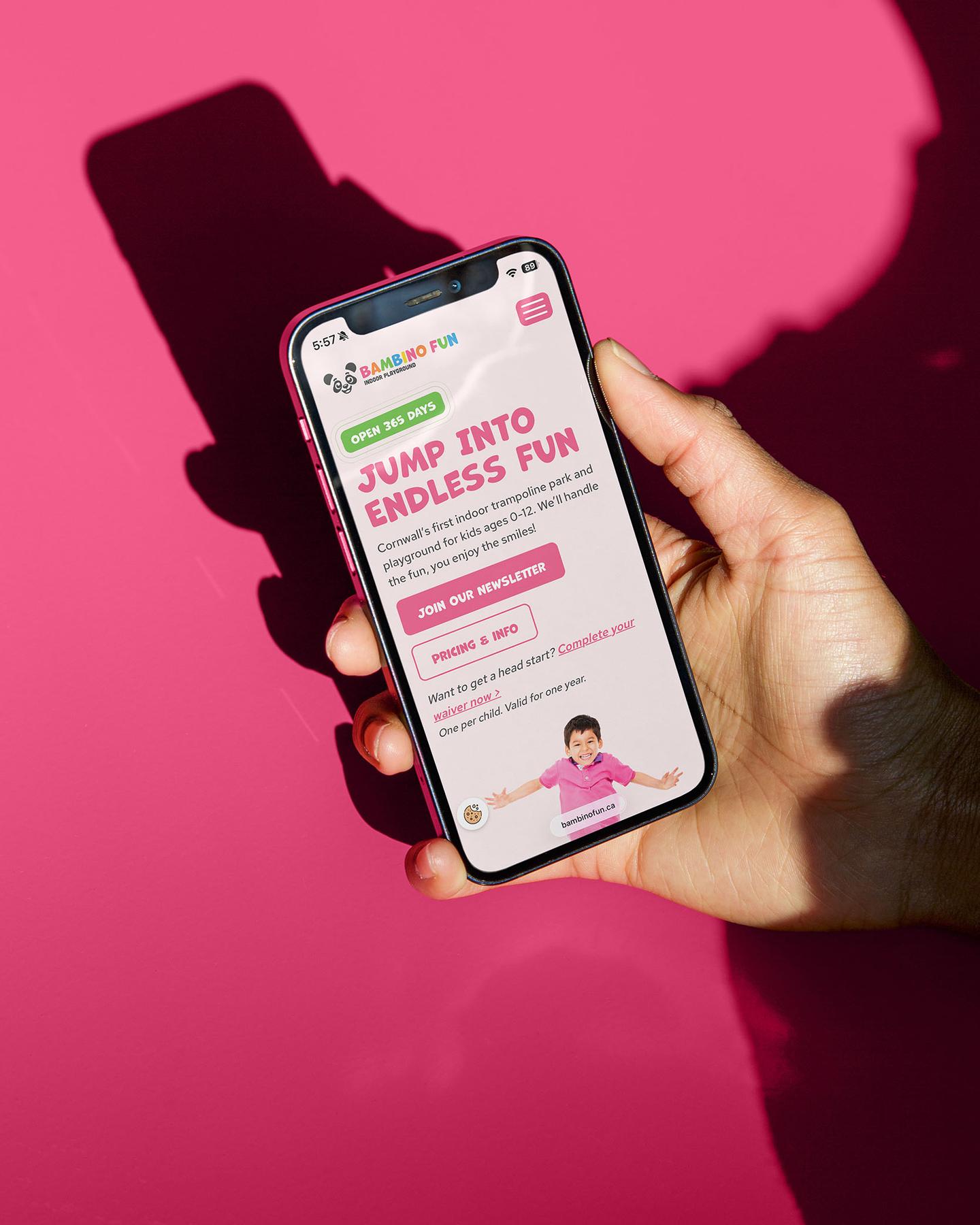 Person holding a phone with the Bambino Fun website home page open with text that reads "Jump into endless fun"