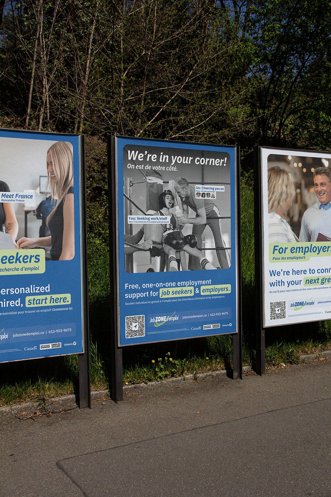 Exterior posters for job zone d'emploi featuring one for job seekers, one for employers, and one in the middle that says we're in your corner and has a visual of a coach and a boxer in their boxing ring corner. 