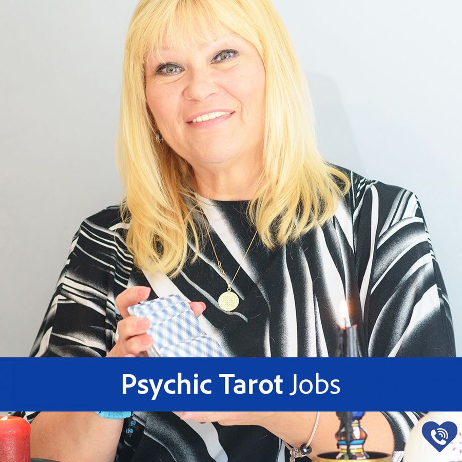 A female psychic reader, sitting down and smiling whilst shuffling her deck of tarot cards.
