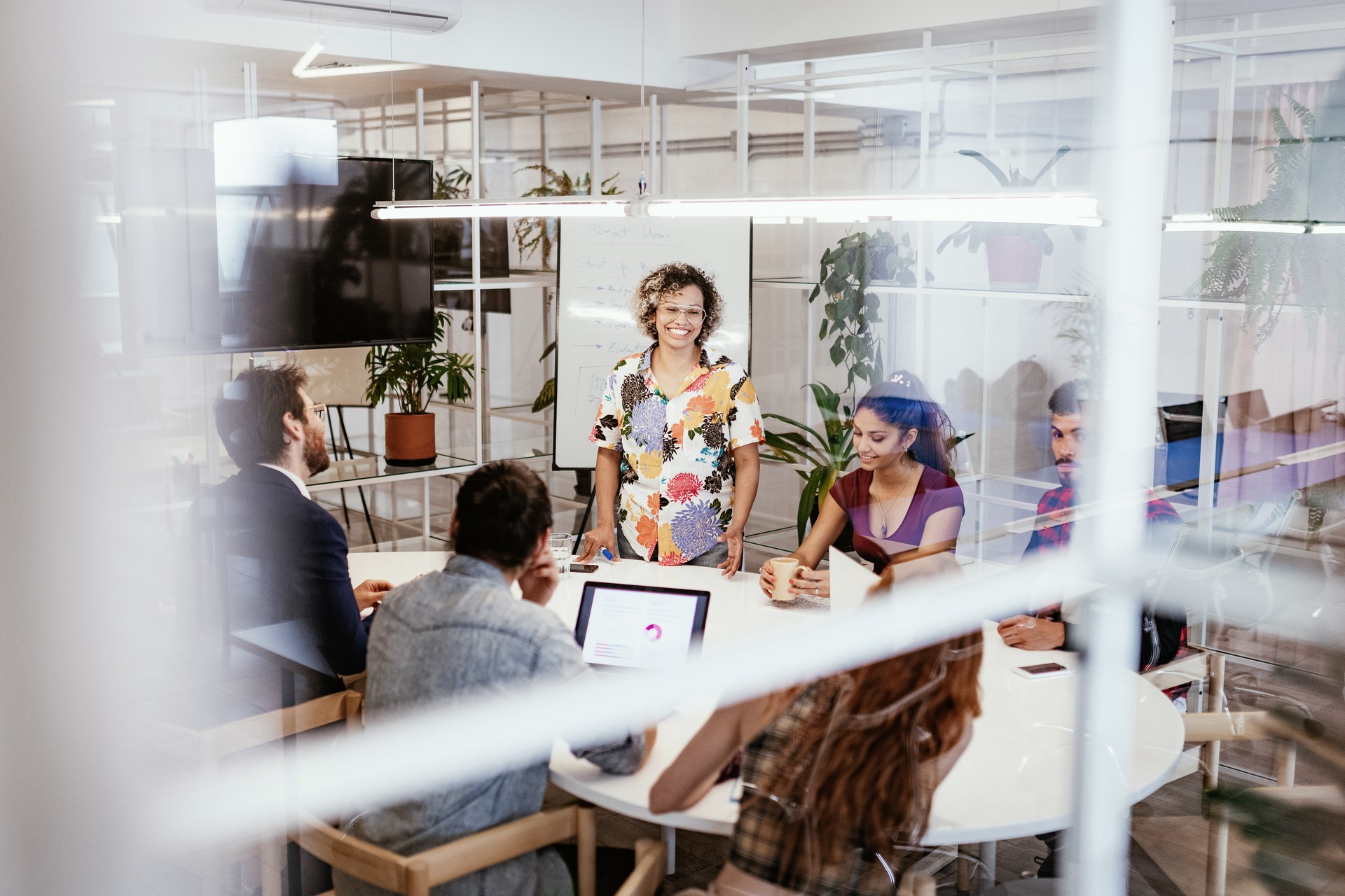 A smiling woman stands with diverse colleagues at a meeting table in a modern office.