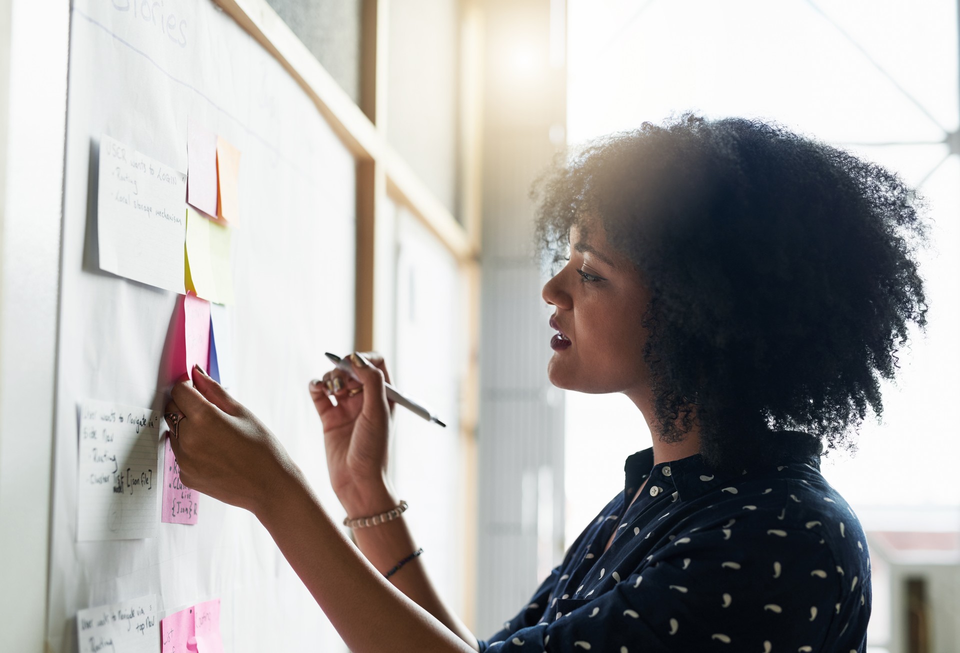 A woman places a sticky note on a board, holding a pen.